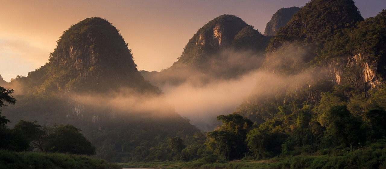Karst mountains in warm mist above a quiet river.